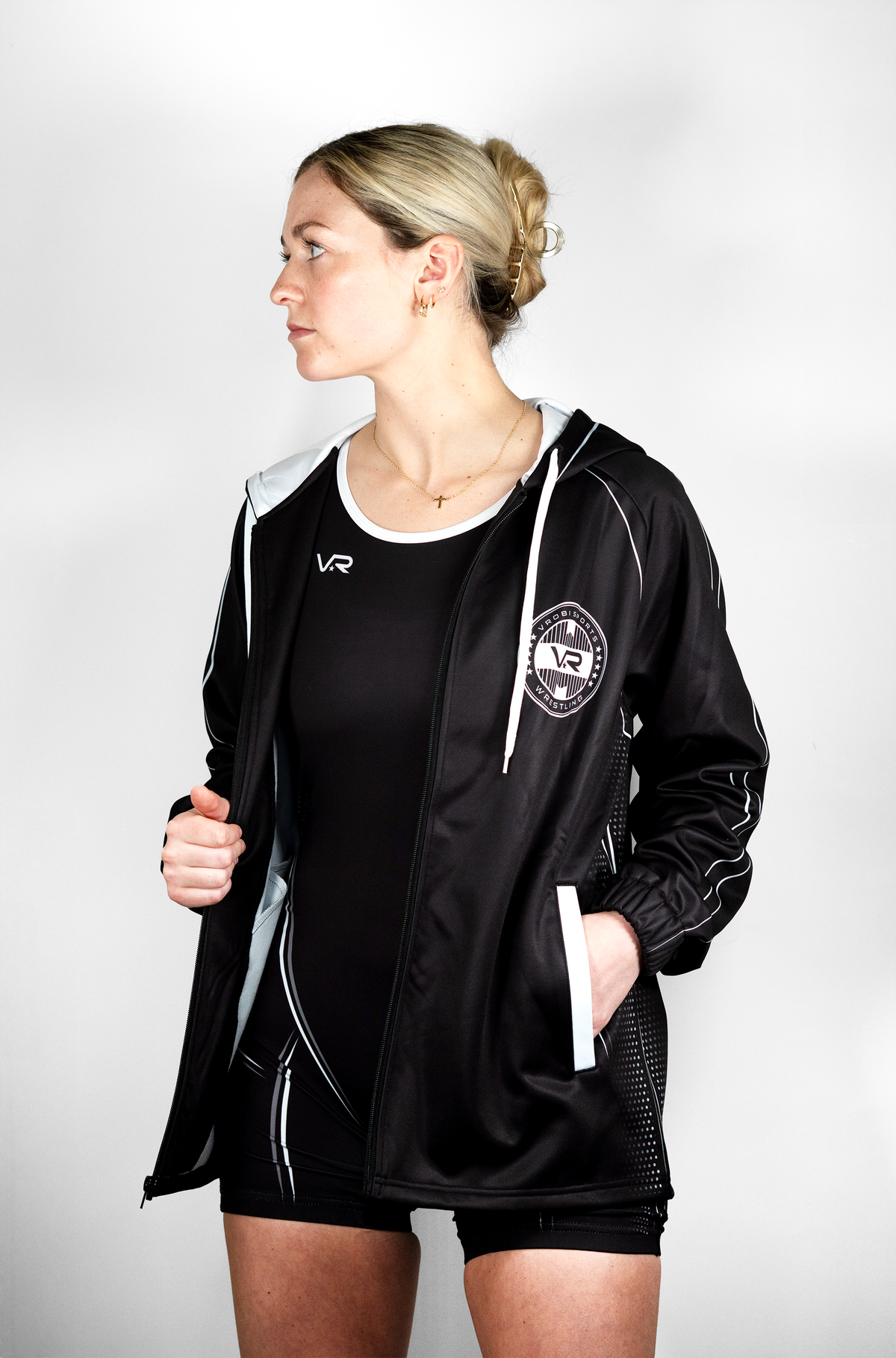 A woman wearing a black wrestling warmup full zip with a hood and white details, including a logo on the chest.