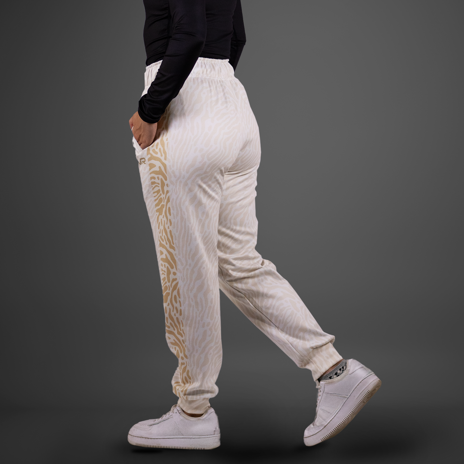 Person wearing white jogger pants with a gold pattern and white sneakers on a dark background