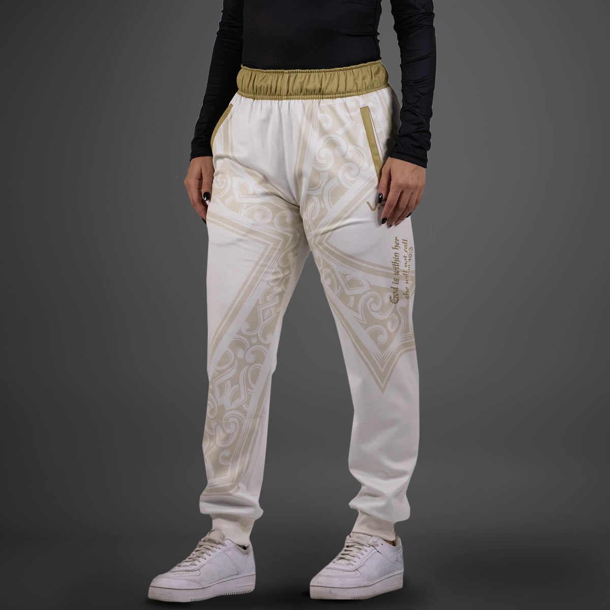 White jogger pants with gold patterns worn by a person on a gray background