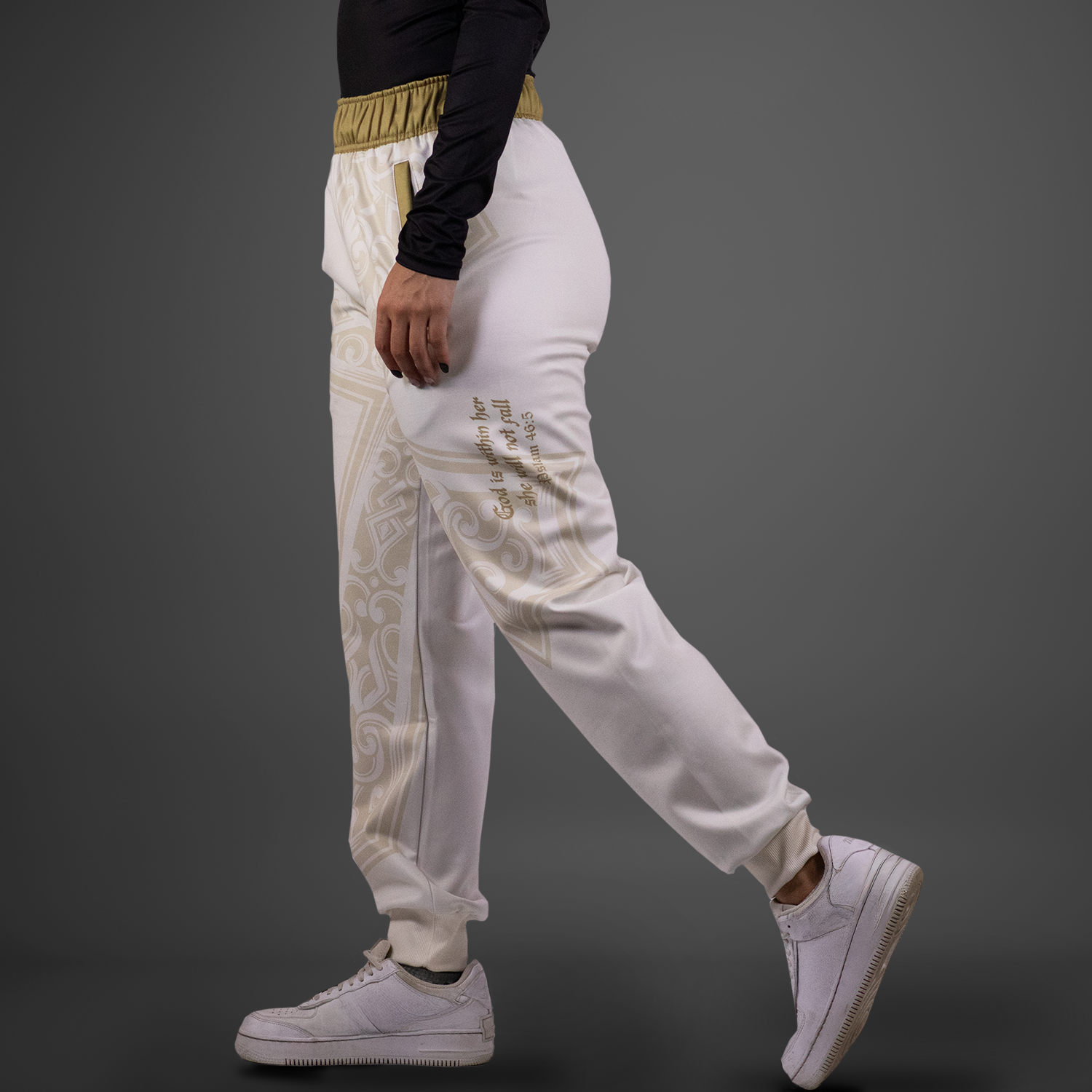 Person wearing white pants with gold patterns and white sneakers on a dark background