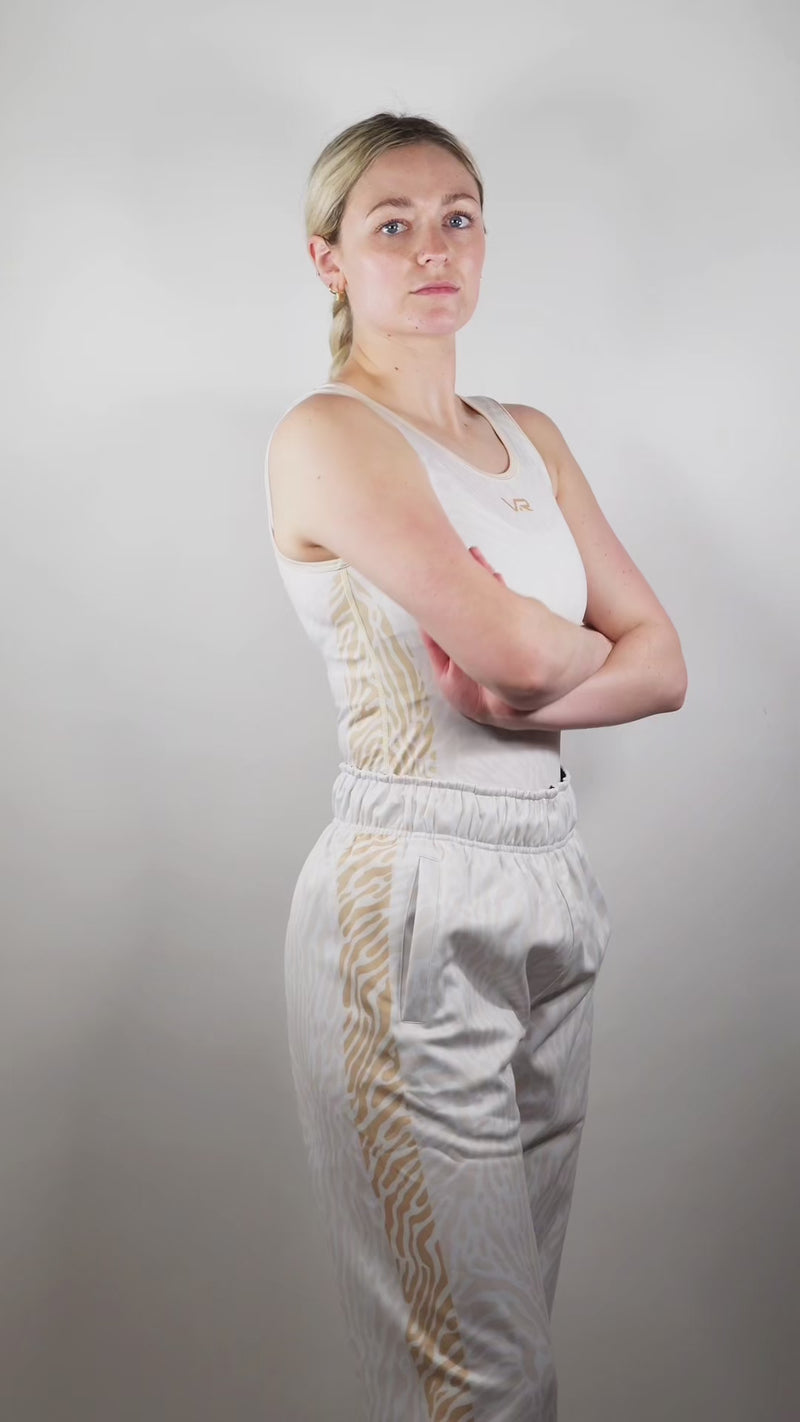A girl in a wrestling singlet and wrestling full zip hoodie and joggers in front of a grey background.